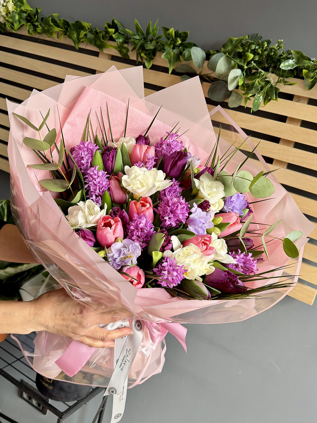 Buchet Lovely Day cu zambile mov, frezii albe, lalele roz și mov, eucalipt și beargrass în ambalaj roz pastel cu panglică