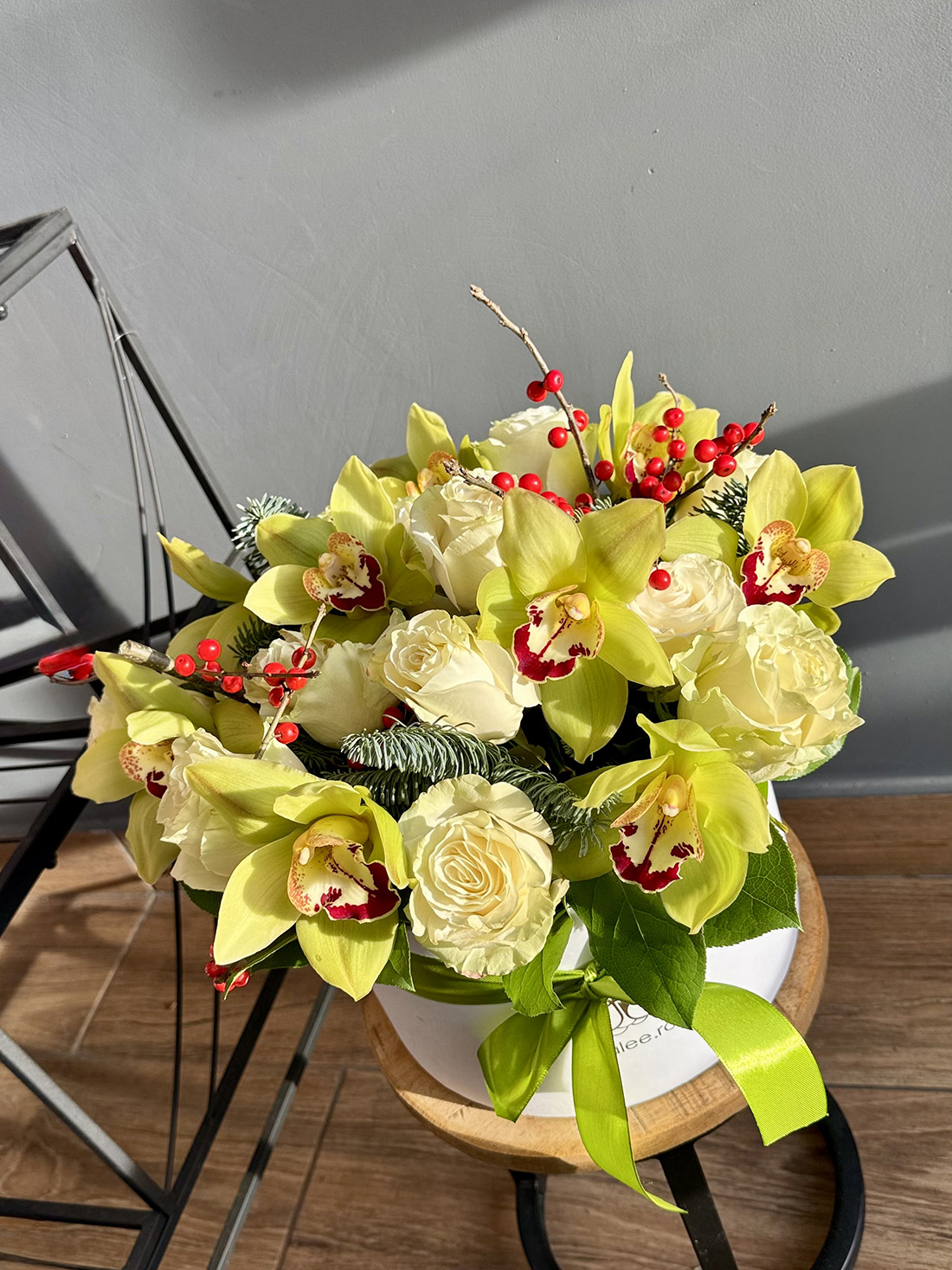 Aranjament de iarnă cu trandafiri crem, cymbidium verde, brad și ilex roșu, în cutie rotundă, livrare flori Iași