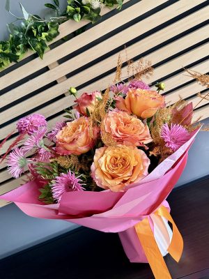 Buchet Mango Dream cu trandafiri portocaliu-corai, germini mov-roz și astilbe ruginii în ambalaj roz vibrant cu panglici